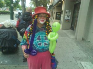 Dozo the Clown on her way to the Berkeley Farmer's Market on a Saturday in July, with a balloon alien and a balloon "sword."